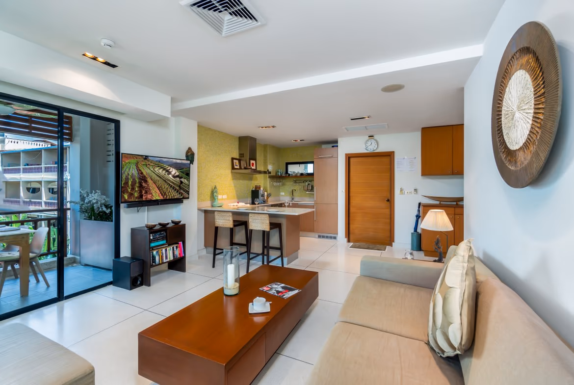 A modern living room with a sofa, coffee table, and an open layout connecting to a kitchen and dining area.