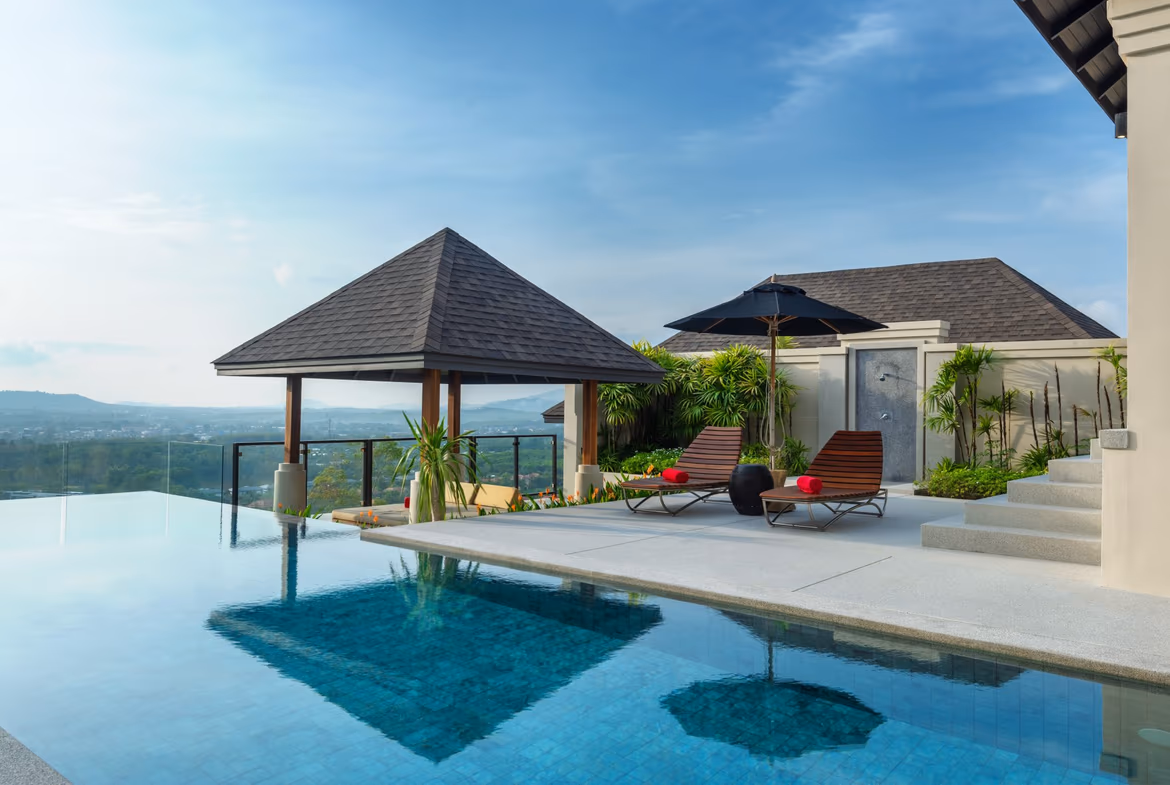 An outdoor infinity pool overlooks a lush green landscape with distant mountains.