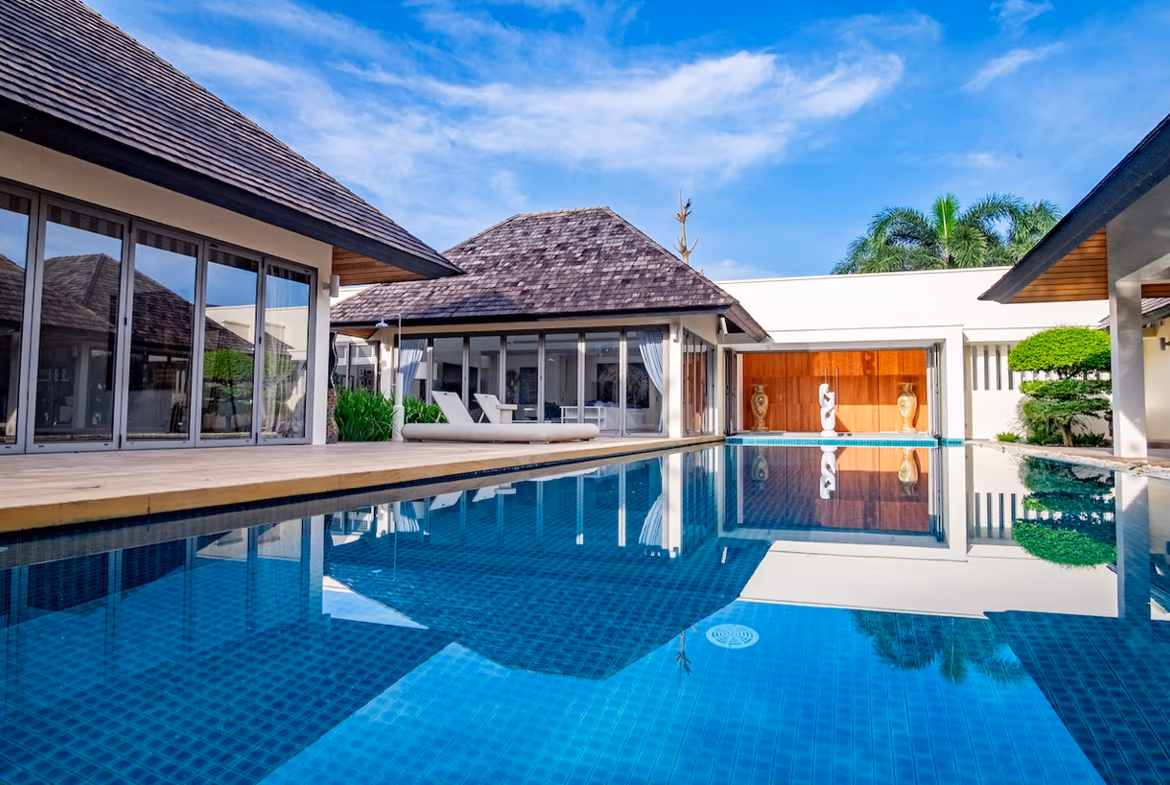 A modern five-bedroom villa in Cherngtalay features a large swimming pool. The property includes a spacious outdoor living area with views of the surrounding landscape.