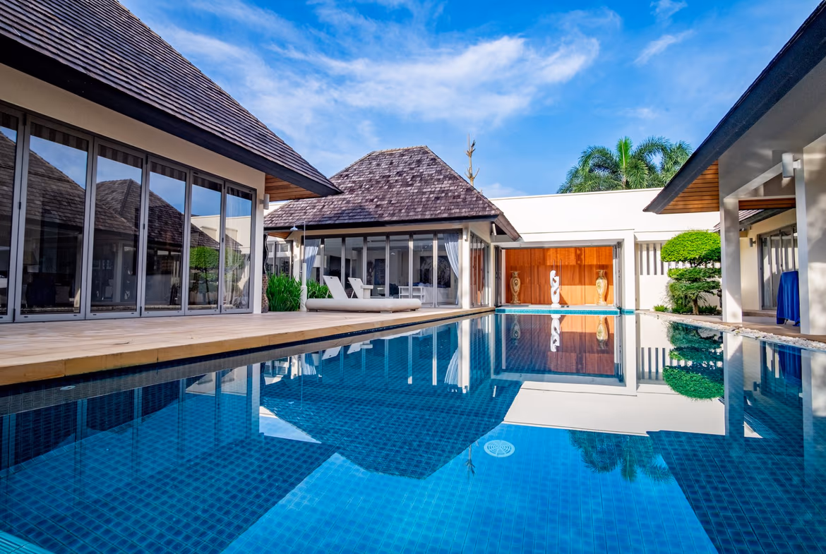 A spacious living area with modern furnishings and a large window overlooking a garden with a swimming pool.