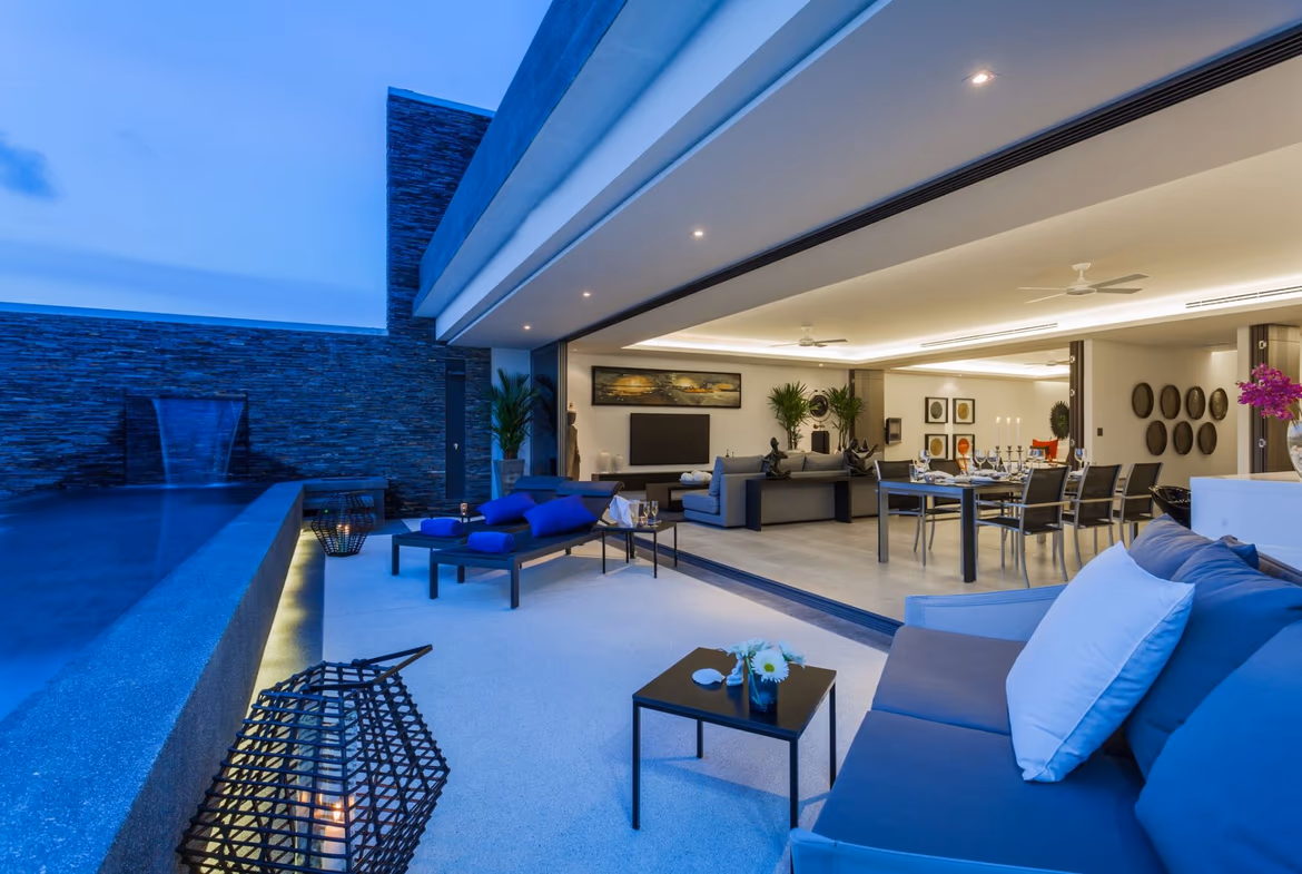 A spacious living room features modern furniture, high ceilings, large windows, and a view of the ocean.