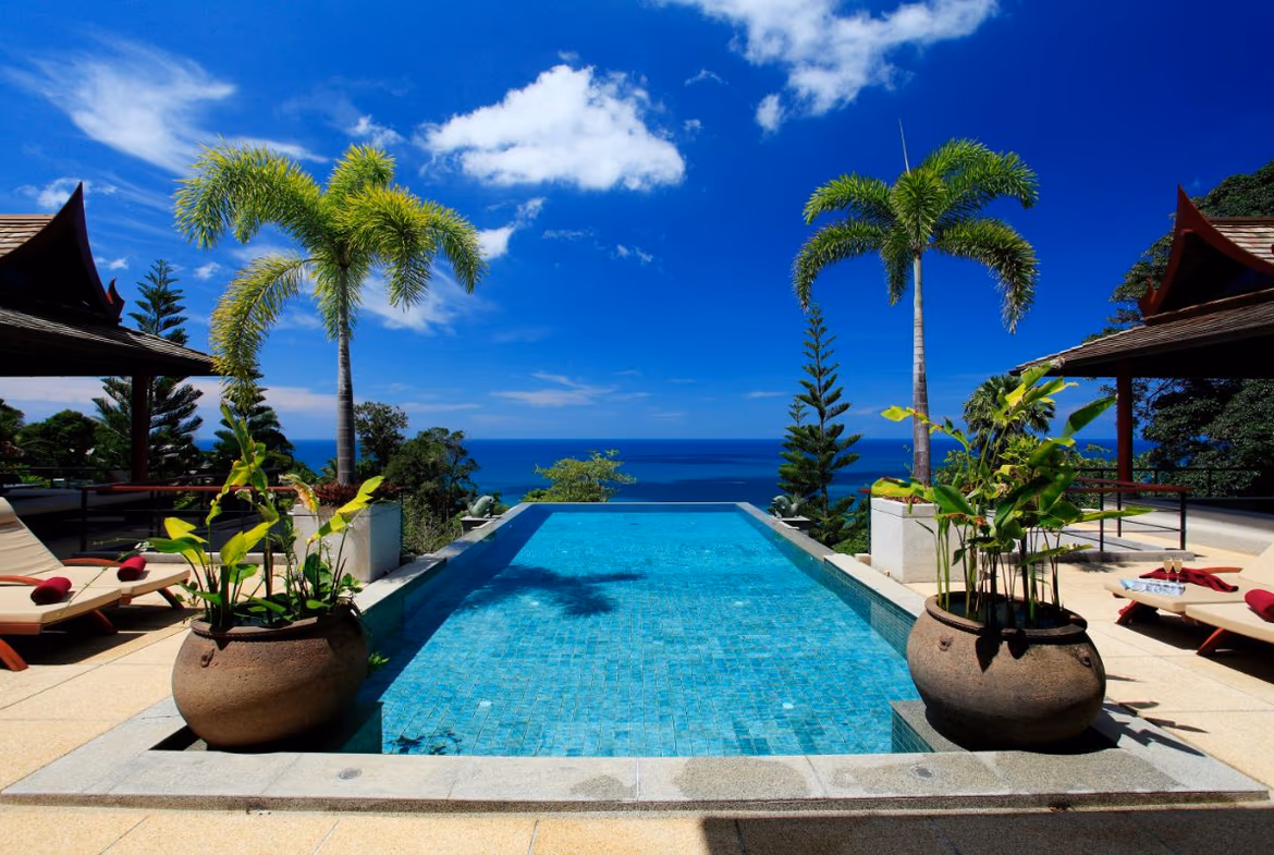 A six-bedroom luxury villa in Bang Tao with expansive ocean views. The multi-story white building features several balconies and a large infinity pool.
