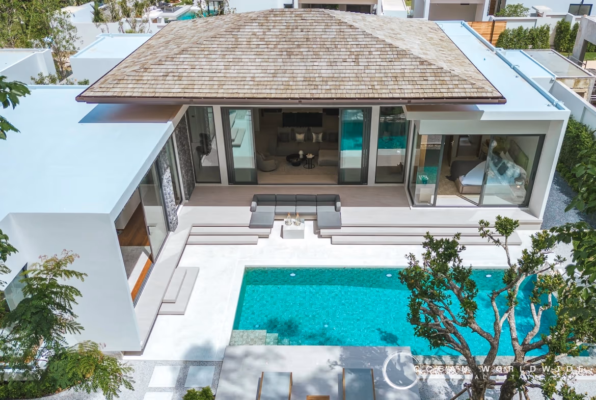 A modern villa in Bang Tao with a private pool. The exterior photo shows a multi-story building with clean lines and large windows, surrounded by tropical landscaping.
