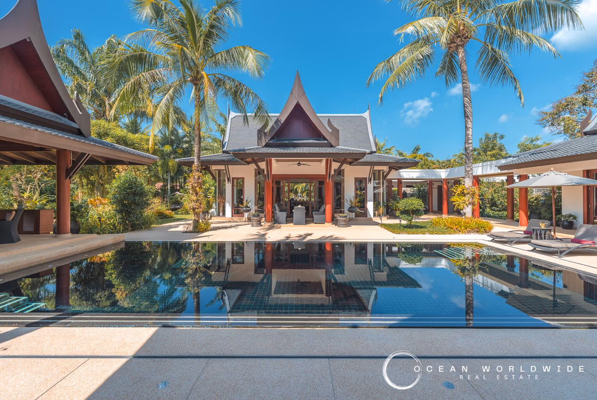 A large white villa with a red tile roof and a private swimming pool, surrounded by tropical landscaping.