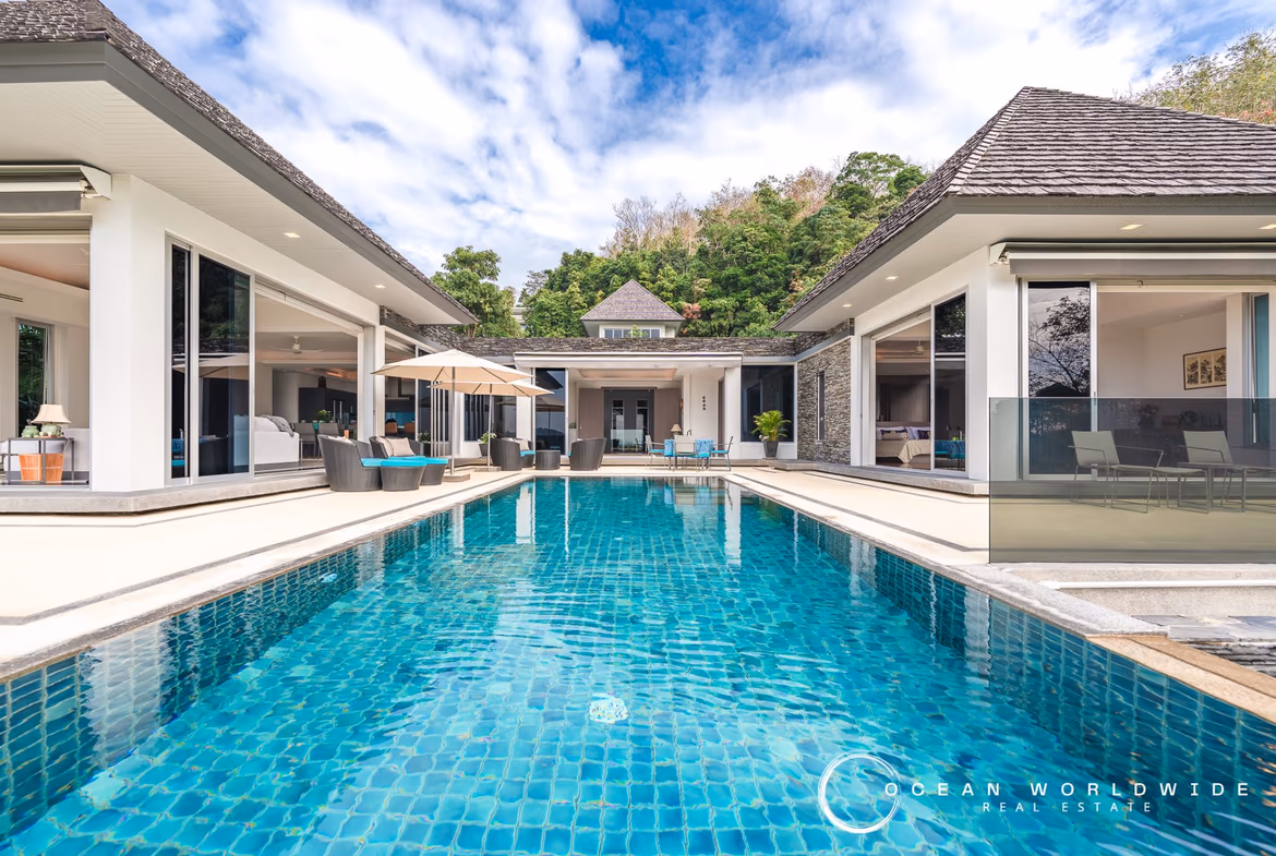 An infinity pool with dark tile overlooks a hillside and ocean.