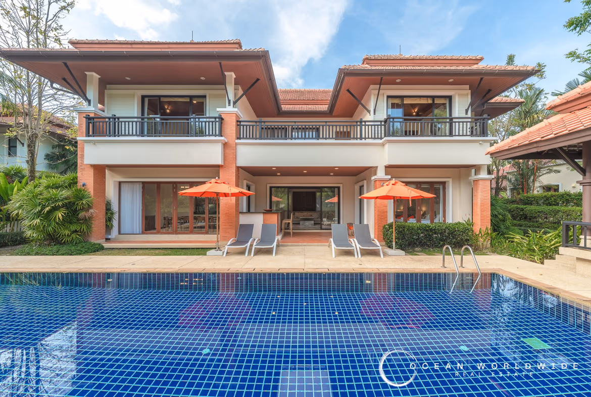 A four-bedroom villa in Bang Tao, Thailand, featuring a large lake in the background. The modern villa has a flat roof and a private swimming pool.