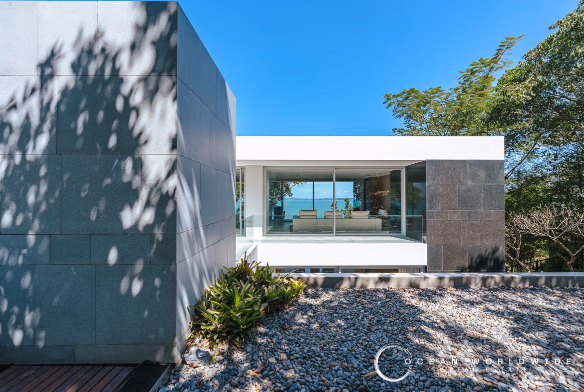 A modern, spacious living area with minimalist decor opens to an outdoor patio and swimming pool overlooking the ocean.