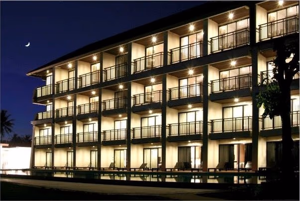 A modern hotel room with a balcony offering a view of the ocean and palm trees.