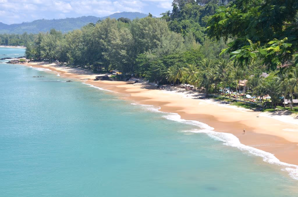 An aerial view reveals a beachfront resort with white sand and clear turquoise water.