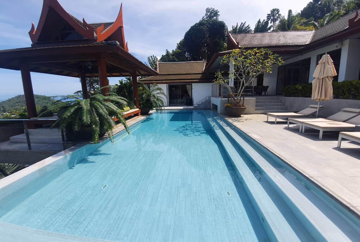 An outdoor infinity pool overlooks the ocean, with lounge chairs and green foliage bordering the pool deck.