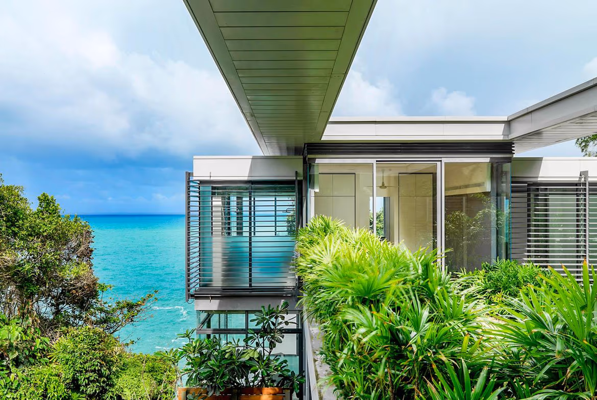 View of a blue swimming pool and the ocean from a villa balcony.
