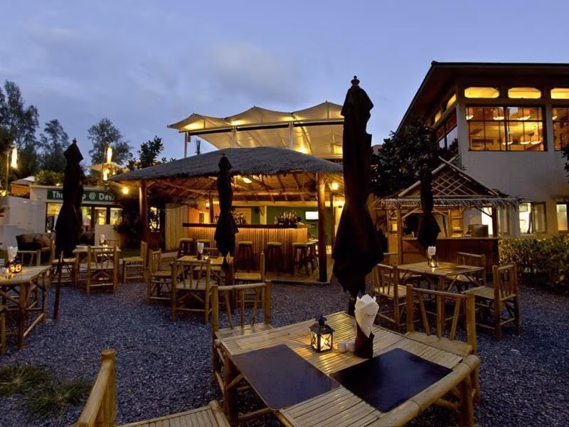 A modern, minimalist hotel room featuring a large bed, wooden furniture, and a private balcony with outdoor seating overlooking a natural landscape.