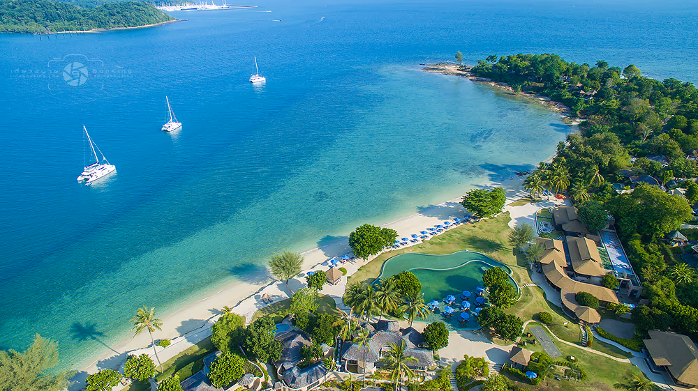 A luxurious beachfront hotel in Phuket features multiple stories and numerous windows. The property is situated directly on a sandy beach.