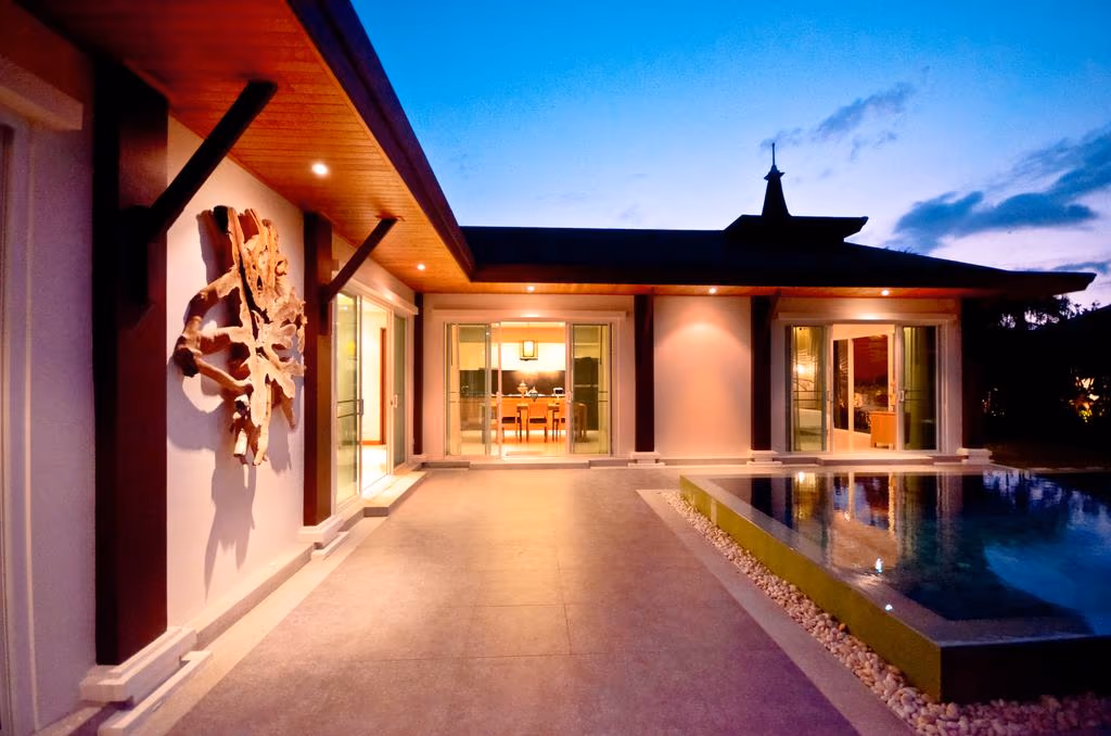 A modern outdoor swimming pool is surrounded by a wooden deck, a hedge, and a white fence.