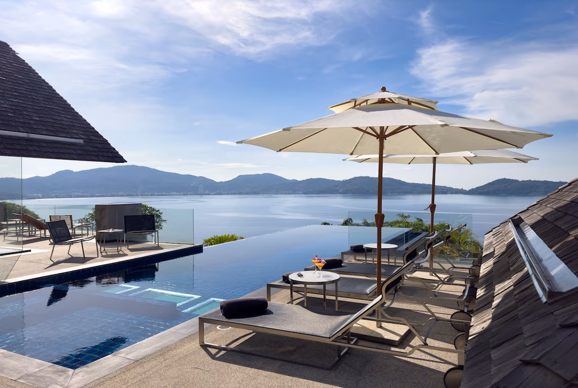 A living room opens onto a balcony overlooking a pool and the ocean.