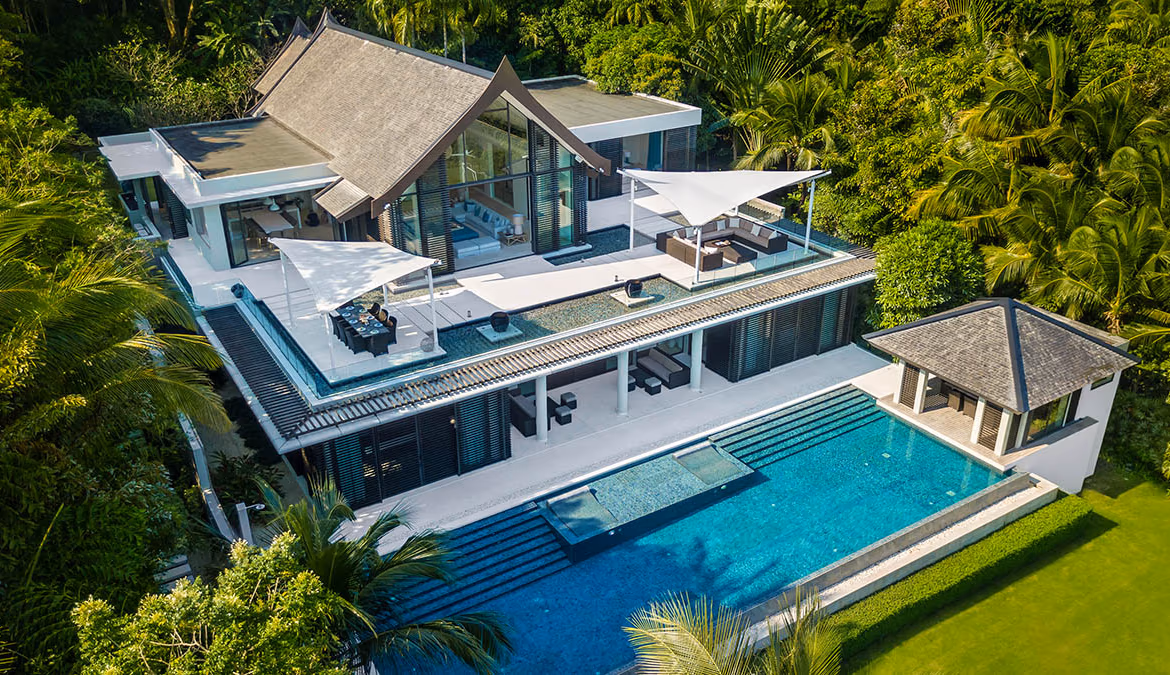 This is a 5-bedroom villa in Cape Yamu, featuring a prominent waterfront location. The multi-story white building has a flat roof and numerous large windows and doors facing the water.
