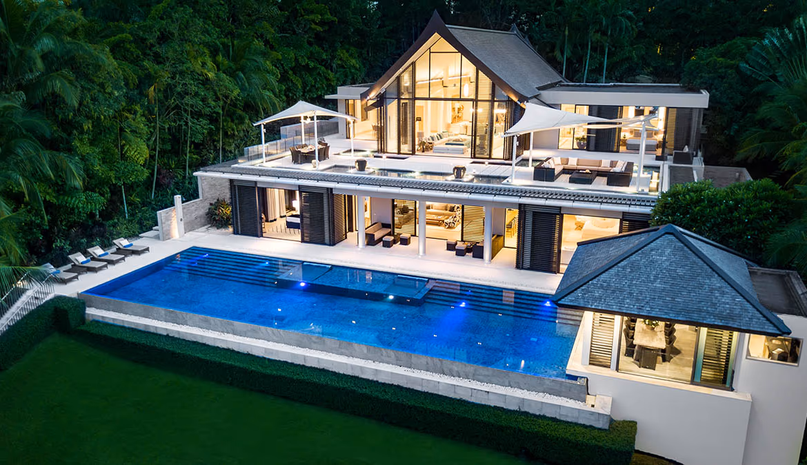 An infinity pool overlooks a serene bay, with a secluded beach and lush hills in the background.