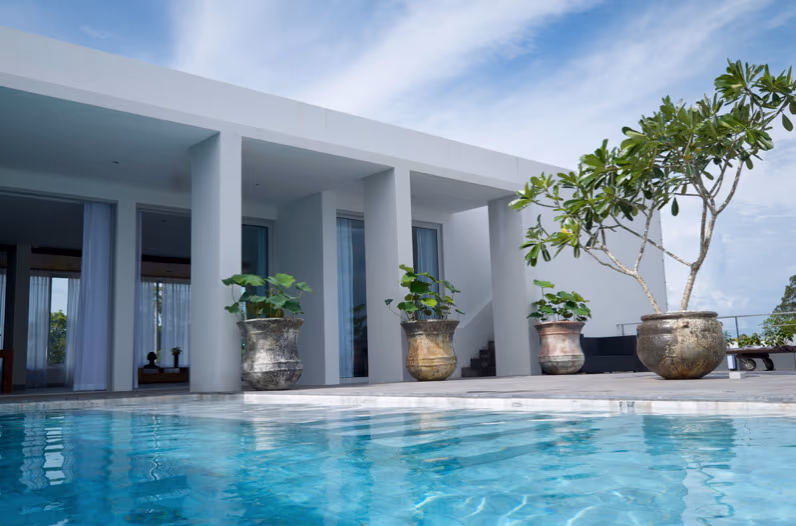 An outdoor patio with a seating area overlooks a tropical garden and the ocean.