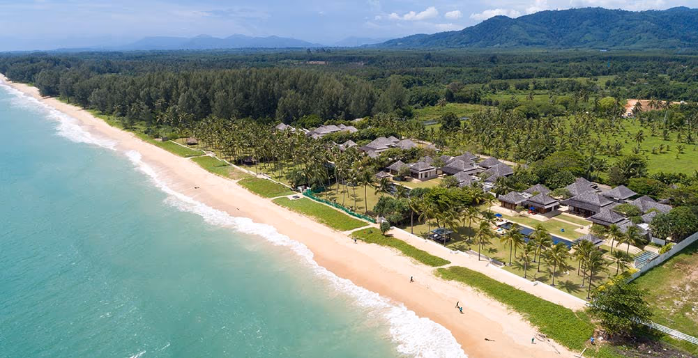 A whitewashed, six-bedroom Natai villa with an asymmetric roof and expansive pool deck, overlooking the ocean.