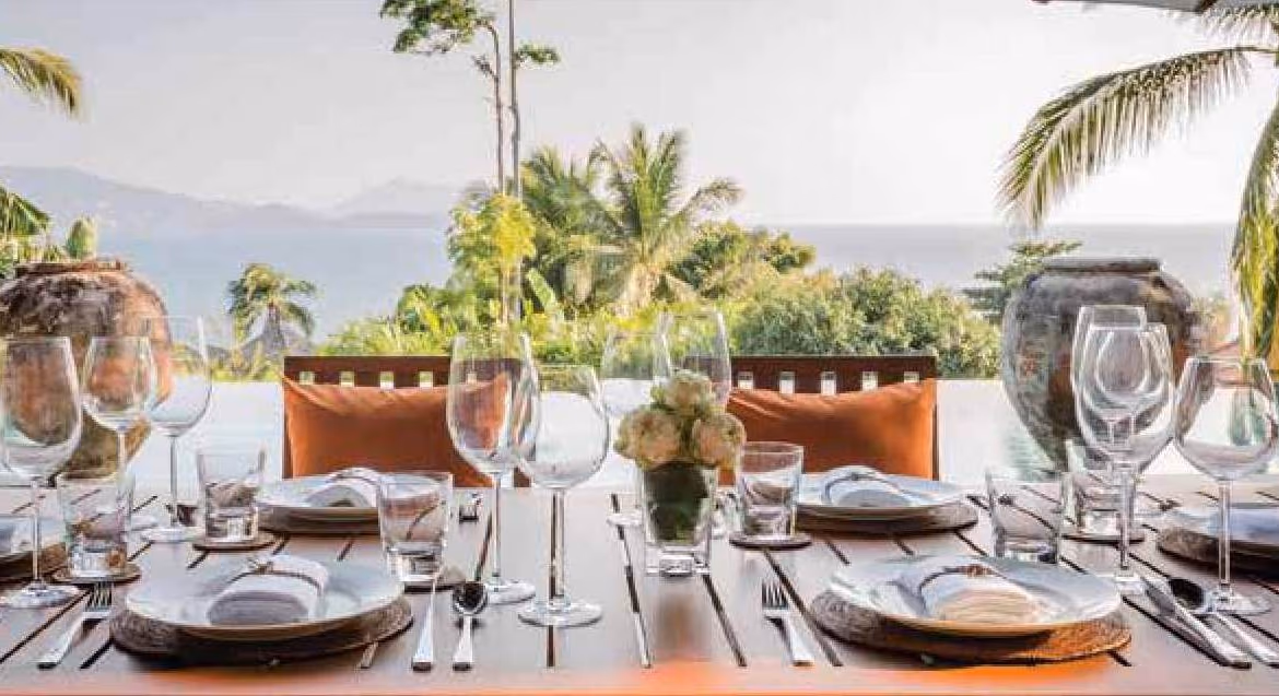 The photo shows a spacious living room with an open layout and modern furnishings, overlooking a private swimming pool and lush tropical greenery.