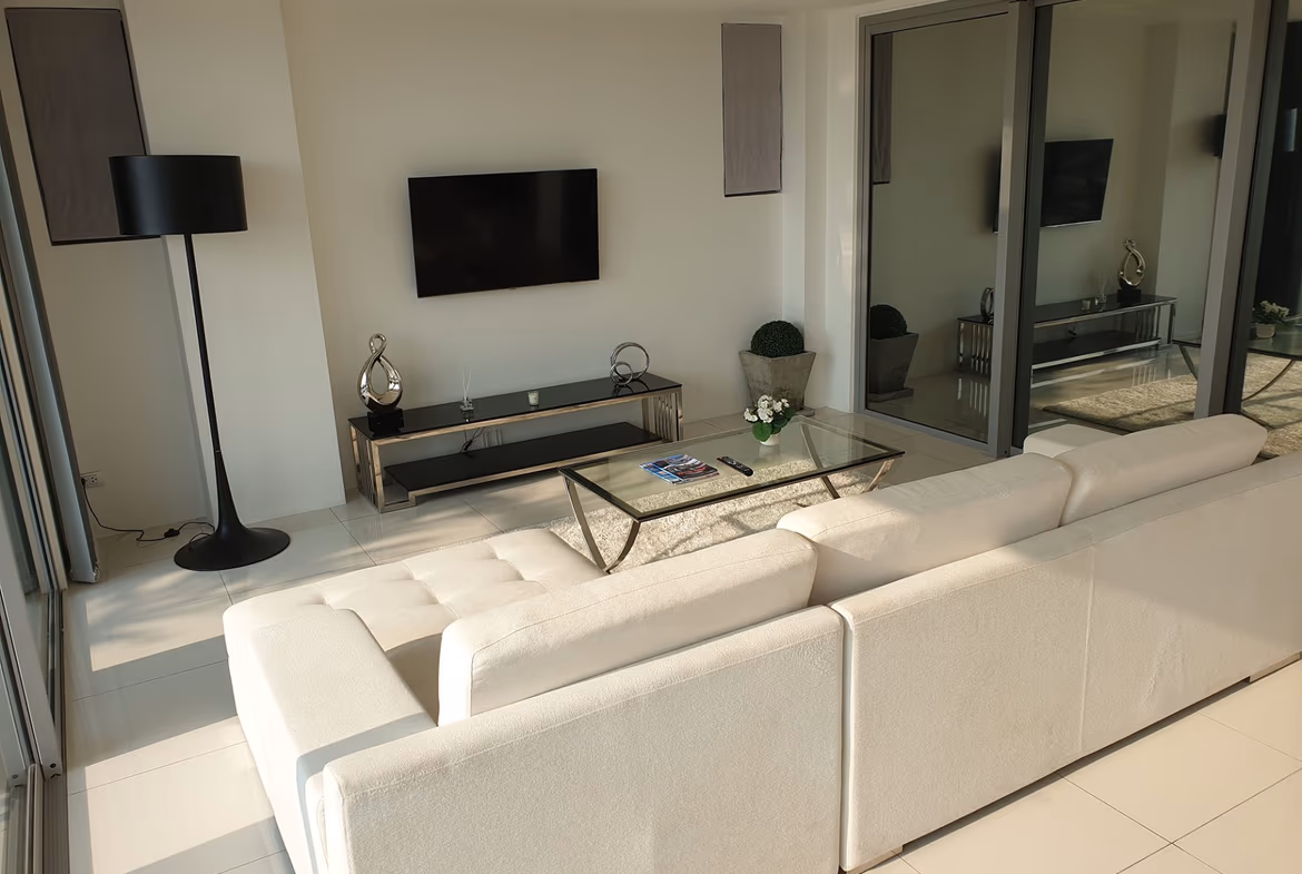 A living room with a brown sofa facing floor-to-ceiling windows with a view of a body of water and distant hills.