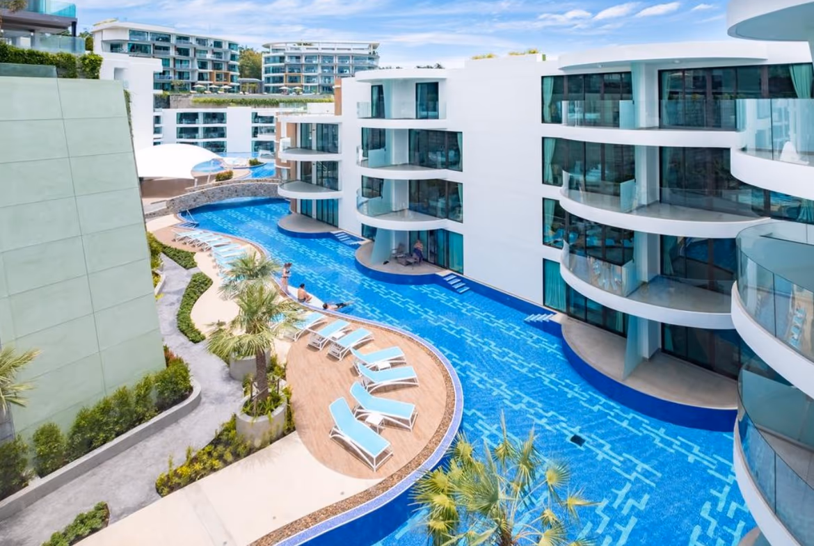 A modern condominium at Patong Beach, Kamala, with a sleek, minimalist design and large windows, surrounded by lush tropical landscaping.