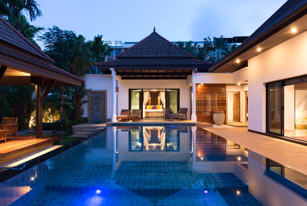 A wide patio with a seating area overlooks a swimming pool and lush landscaping.
