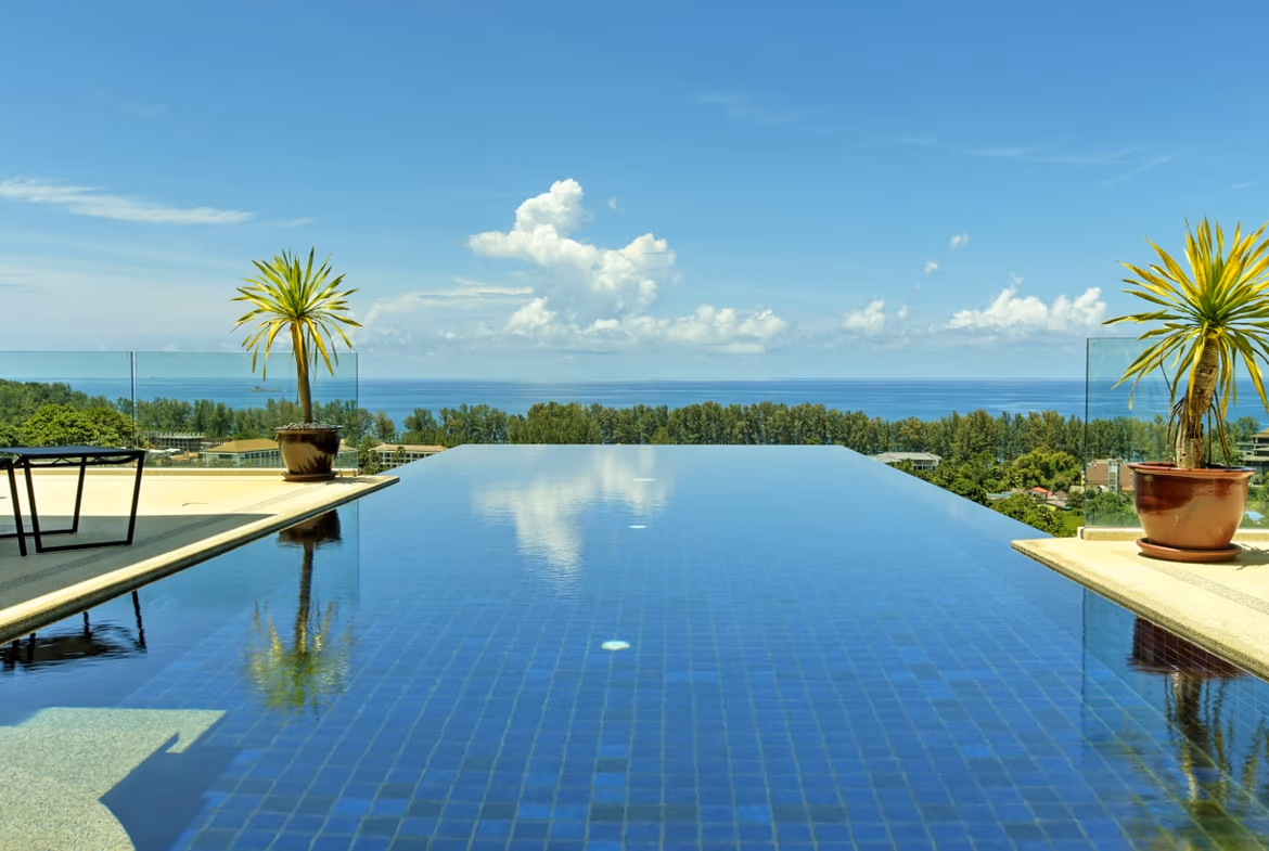 A spacious bedroom with a four-poster bed and hardwood floors, offering a view of the pool and ocean.