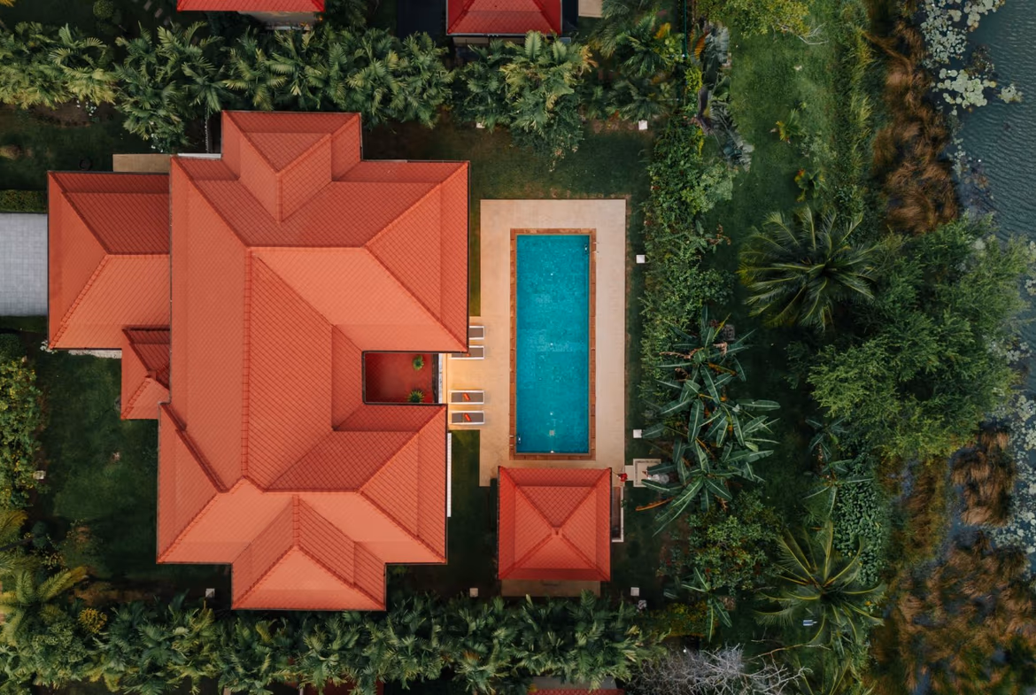 A modern four-bedroom villa in Bang Tao with a private pool and a picturesque lake view. The villa features a clean, white-and-gray exterior with large windows overlooking the water.