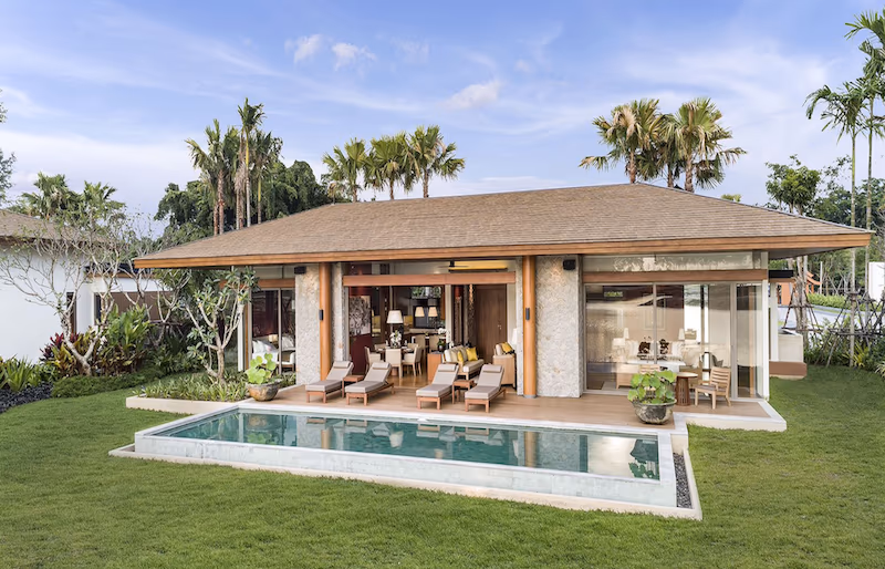 The photo shows a luxury villa in Natai. It features a modern architectural design with a flat roof and large windows overlooking a golf course.