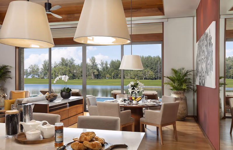 A spacious bedroom with a private balcony overlooking a pool and lush landscape.