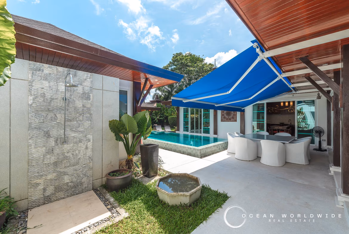 A spacious living room with an L-shaped sofa, coffee table, and a view of the private pool through large glass doors.