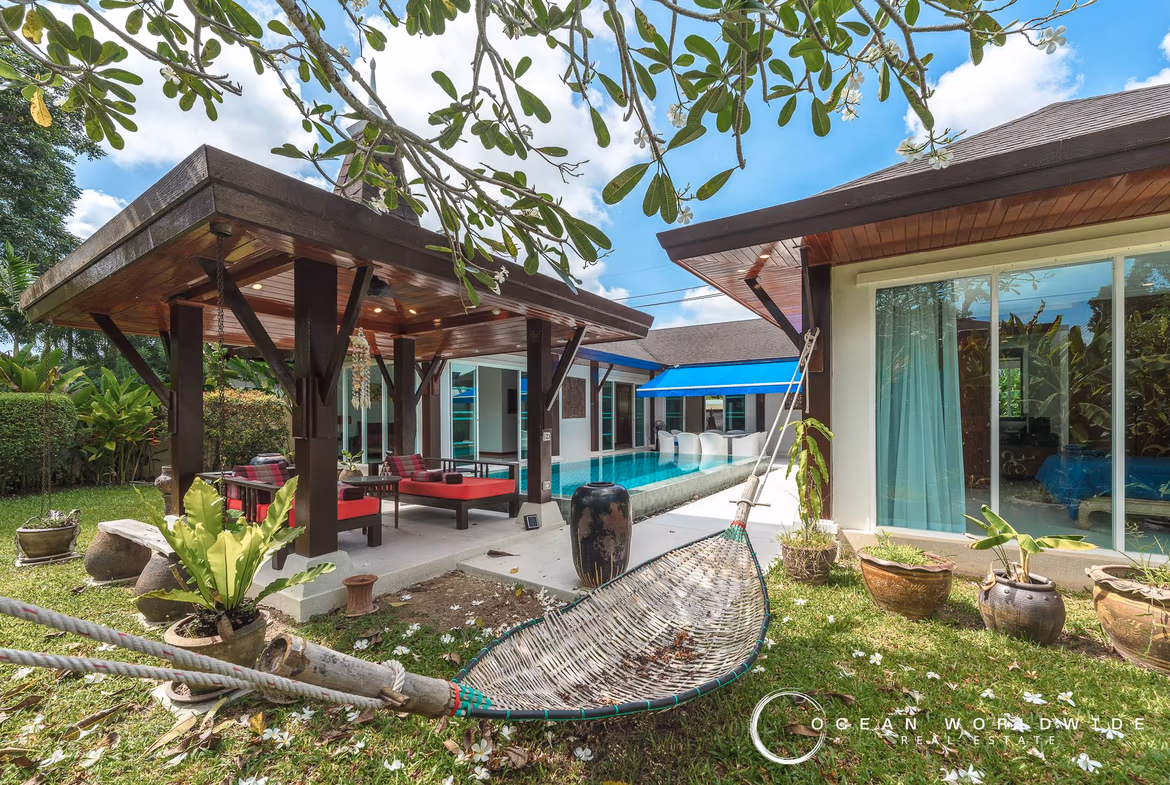 An aerial view shows a modern villa with a swimming pool nestled in a lush green landscape.