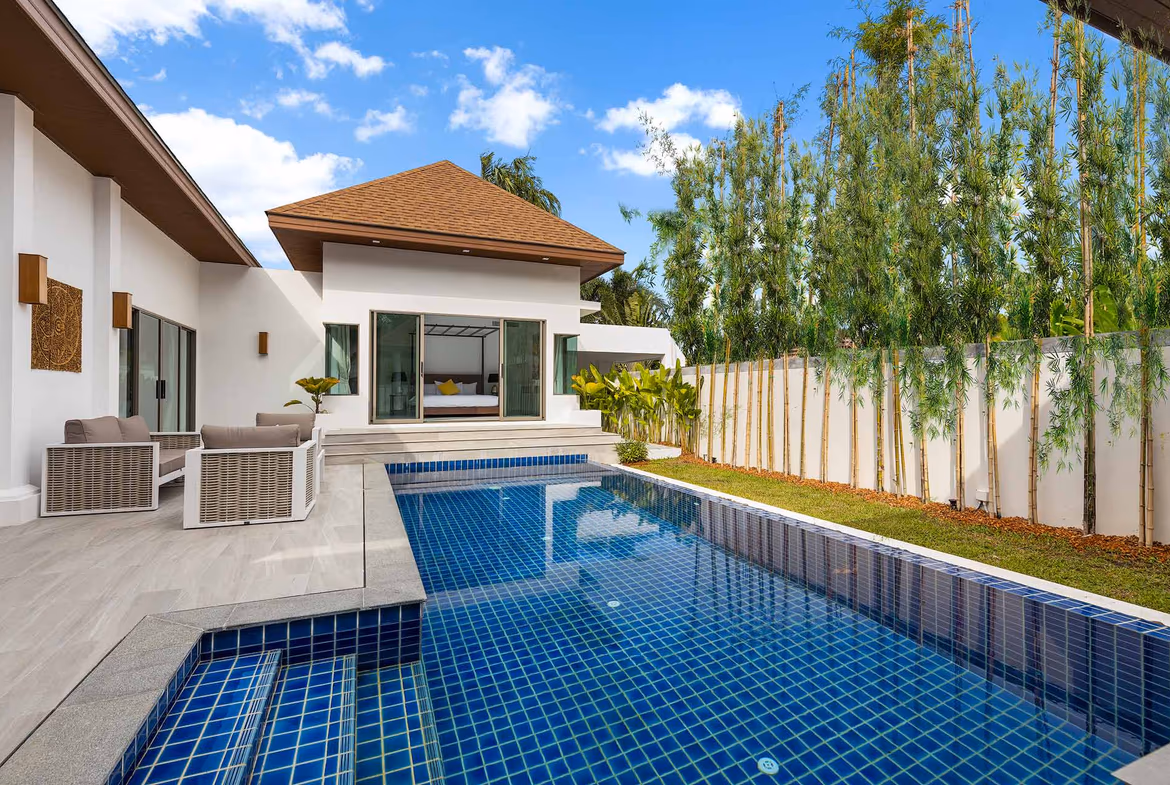 A tiled patio with an outdoor dining table and chairs, overlooking a swimming pool and tropical landscaping.