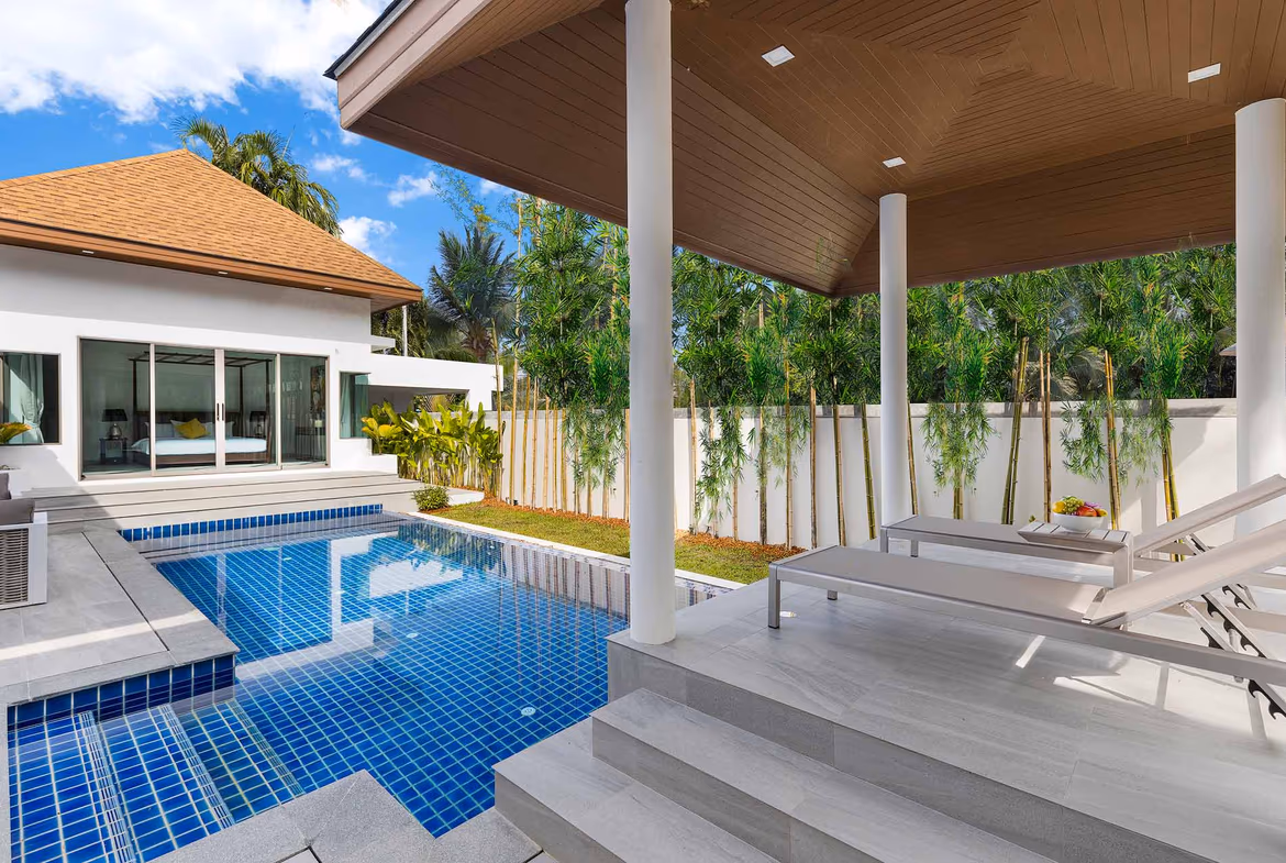 An outdoor patio with a seating area overlooks a swimming pool and a lush garden.