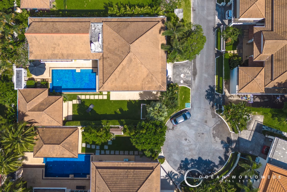 A five-bedroom villa in Koh Kaew features a private pool and a red tile roof. The property is surrounded by palm trees and lush vegetation under a sunny sky.