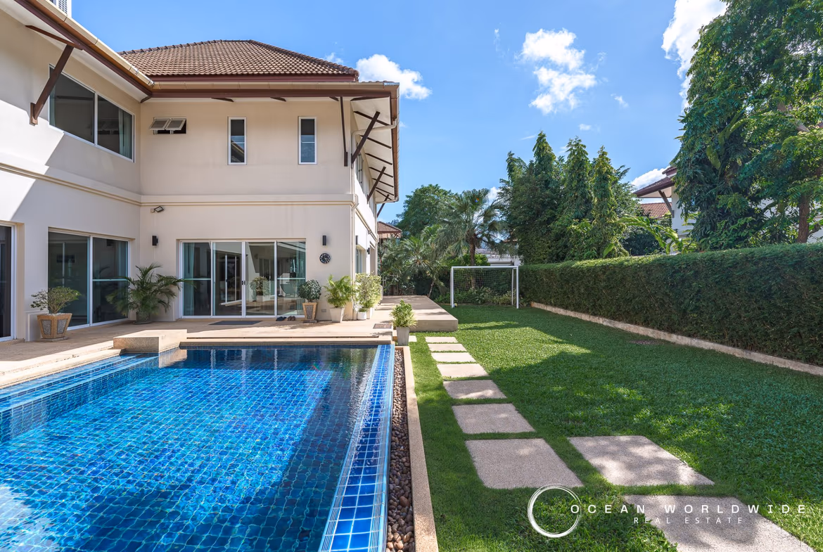 Elevated view of a swimming pool and surrounding patio with distant trees.