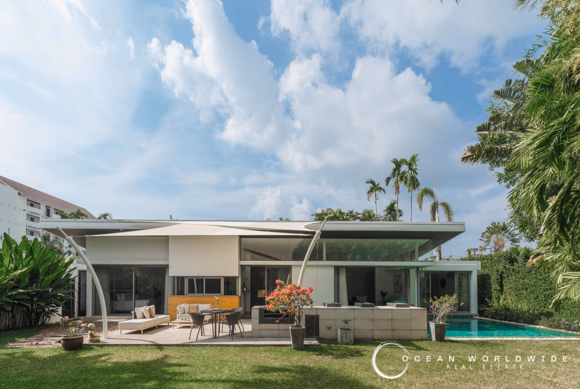 A three-bedroom villa near Layan Beach. The multi-story white building features several balconies with glass railings overlooking a lush, tropical landscape.