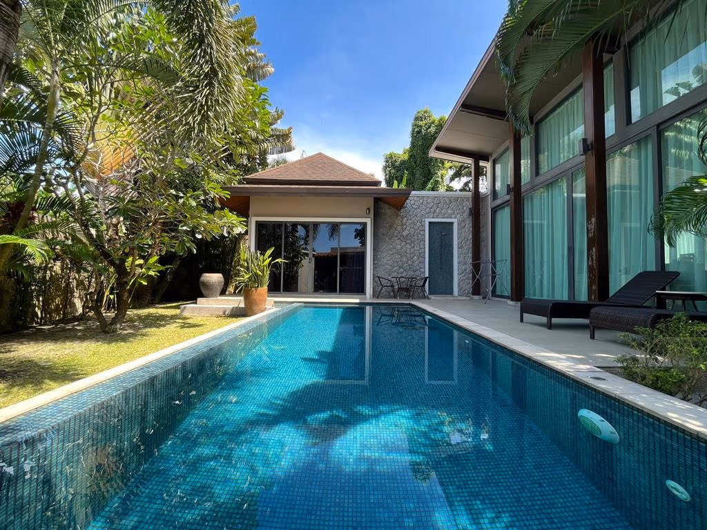 A bedroom with a king-sized bed overlooks a private swimming pool and a lush garden.