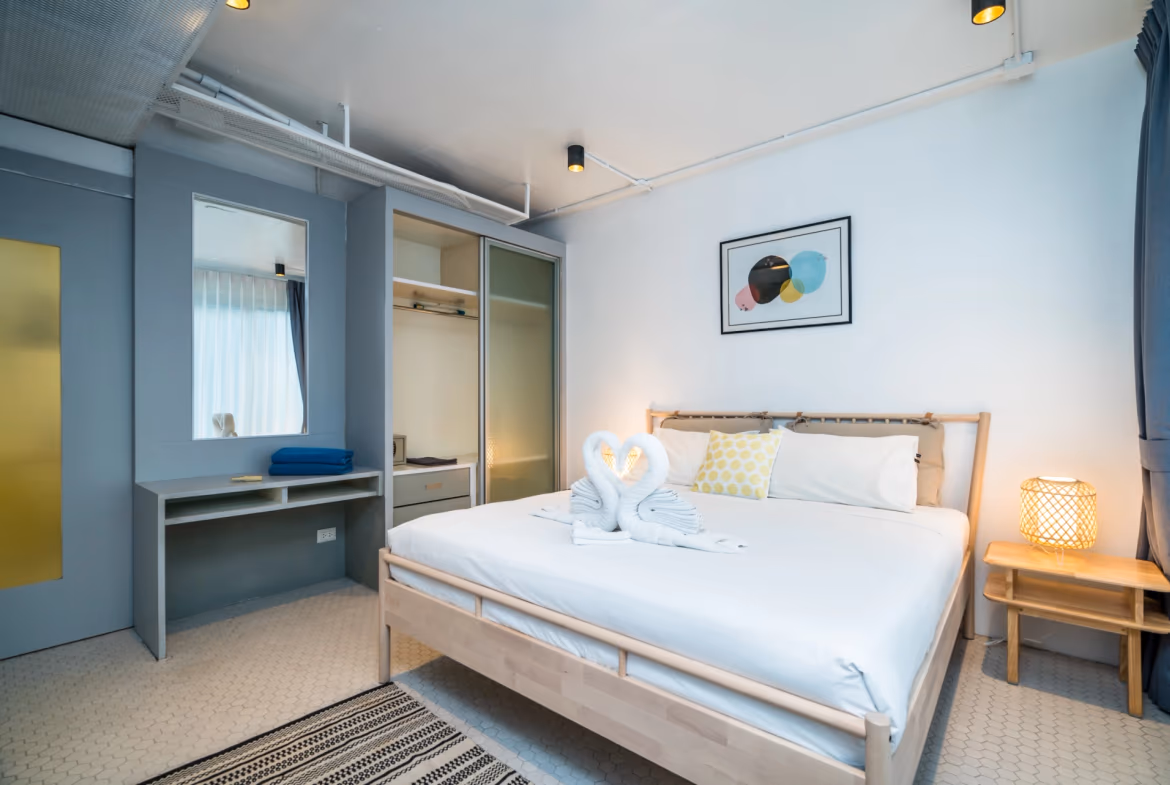 A bedroom with a bed, dresser, and a window overlooking a body of water and hills.