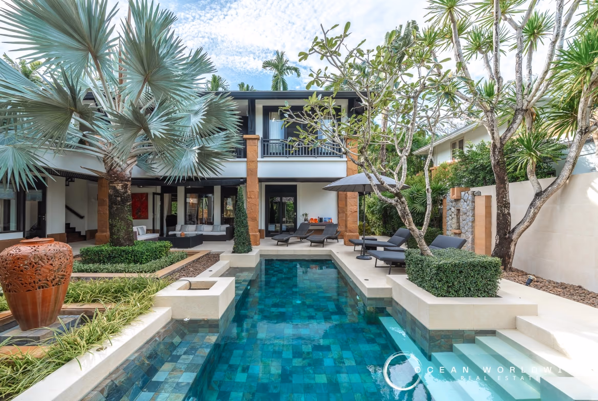 A 3-bedroom villa in Bang Tao with a private pool, viewed from the exterior. The modern building features a flat roof and large glass sliding doors that open onto a patio area.
