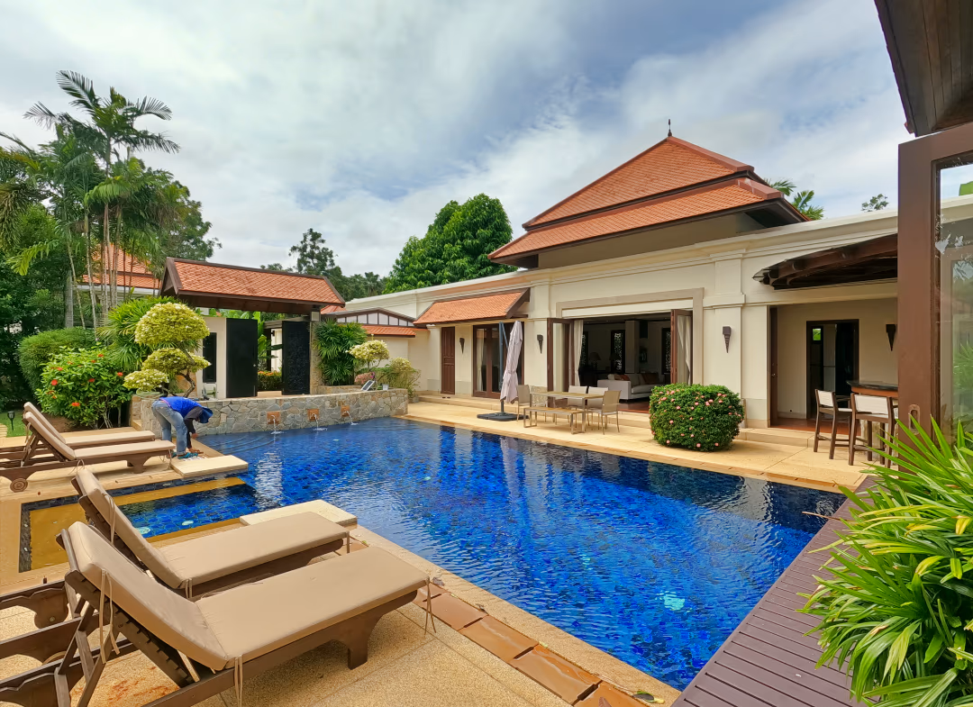 A modern living room with a sectional sofa and a large flat-screen TV, opening to an outdoor patio with a swimming pool.