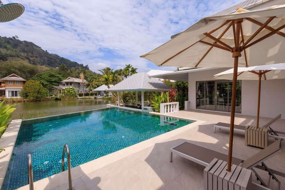 A spacious living room with modern furnishings and large windows overlooks a swimming pool and lake.