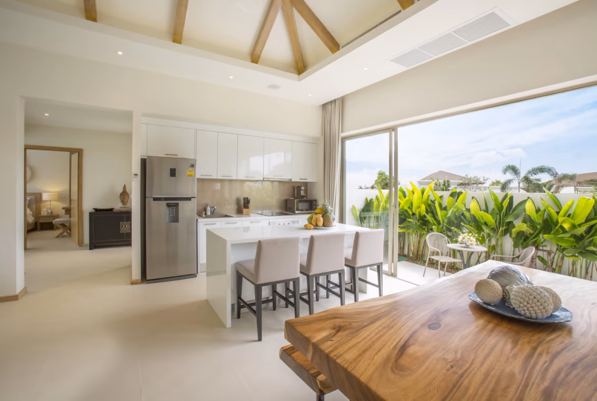 A spacious living room with large glass doors opening to a lush garden and swimming pool.