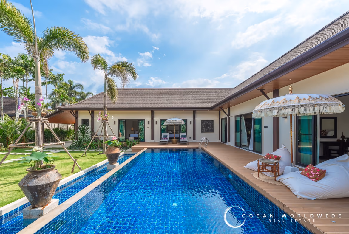 A spacious living room features a dark gray sofa, a large flat-screen TV, and an open layout connecting to a private outdoor pool.
