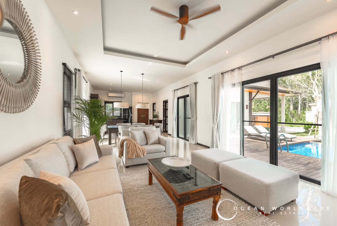 A modern bedroom with a large bed, wooden floors, and a balcony overlooking a pool and lush greenery.