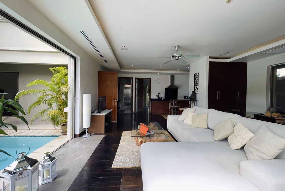 A bedroom features a large, dark wood bed facing a glass door that opens to a private pool and garden.