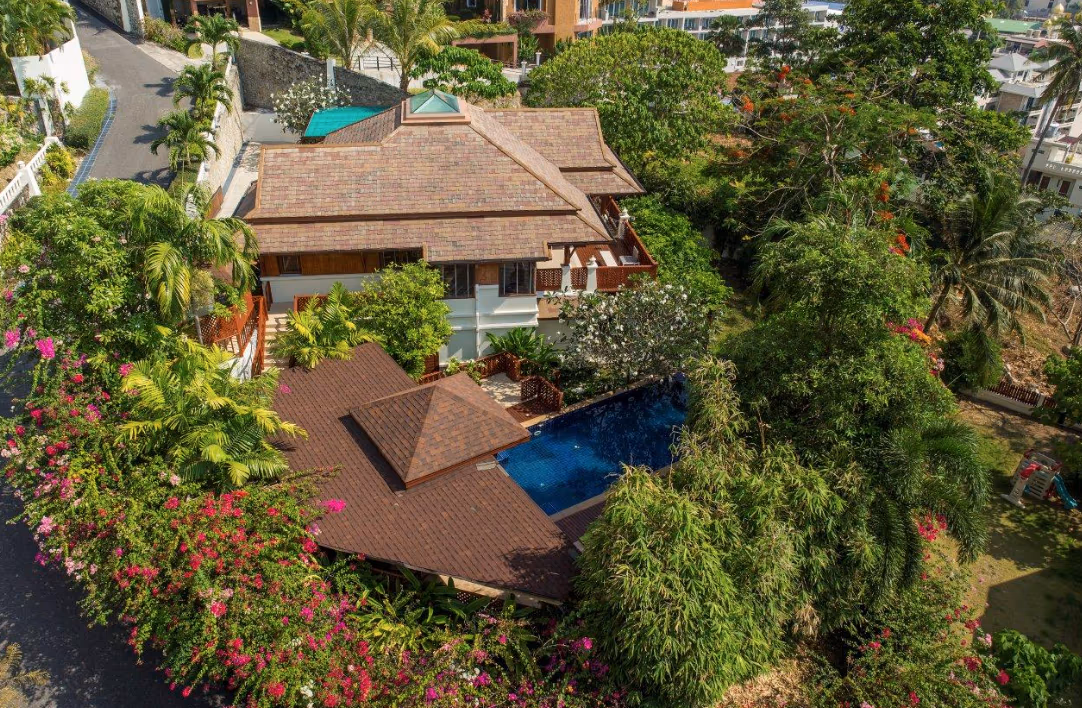 A spacious bedroom with a king-sized bed, high ceilings, dark wood floors, and a private balcony overlooking the ocean.