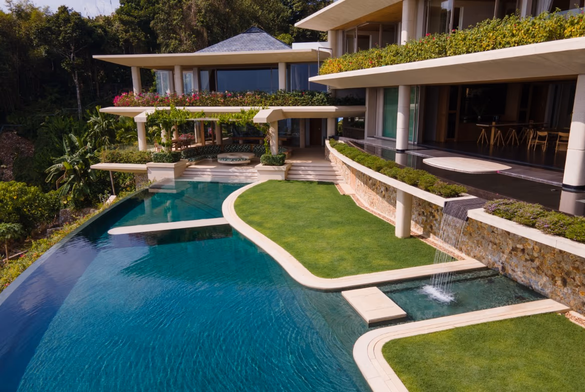 The photo shows a spacious, luxurious living area with a dark wood ceiling and an open view of a patio and the ocean.
