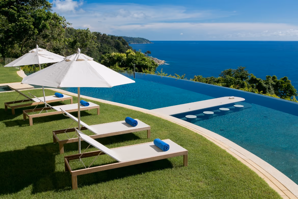 An infinity pool overlooks the ocean from a spacious patio with lounge chairs.
